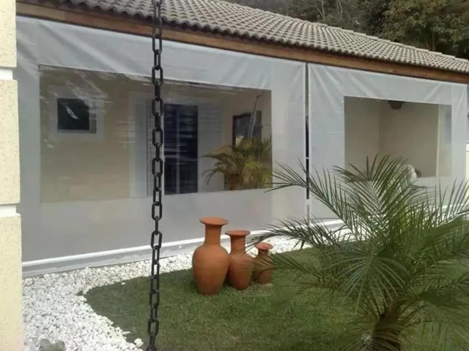 Toldo cortina branco com visor cristal em residência com jardim e vasos decorativos