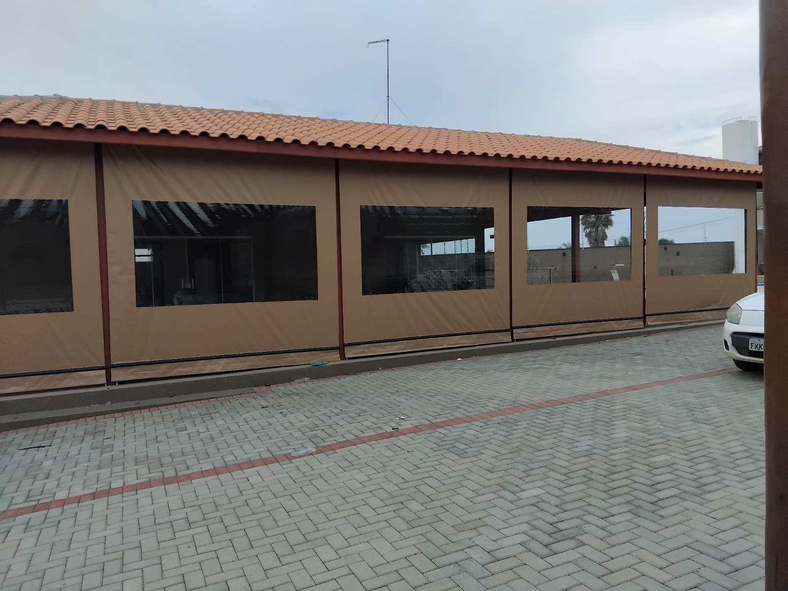 Toldo cortina bege com visores cristal instalado em área externa ampla